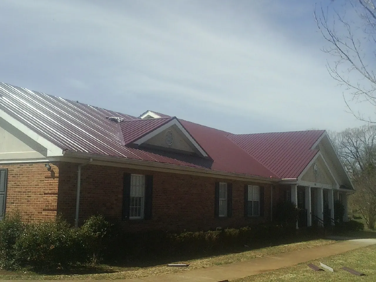 Red metal roof with gabled entries on a long brick building, from a Hail Damage Roof Repair job in Little Rock